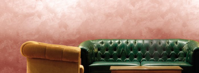 Stylowa skórzana kanapa oraz fotel, a za nimi różowa ściana.
