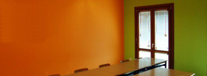 Pomieszczenie przypomina sale konferencyjną z jednym dużym oknem oraz dwoma kolorami ścian - pomarańczowym i oliwkowym.